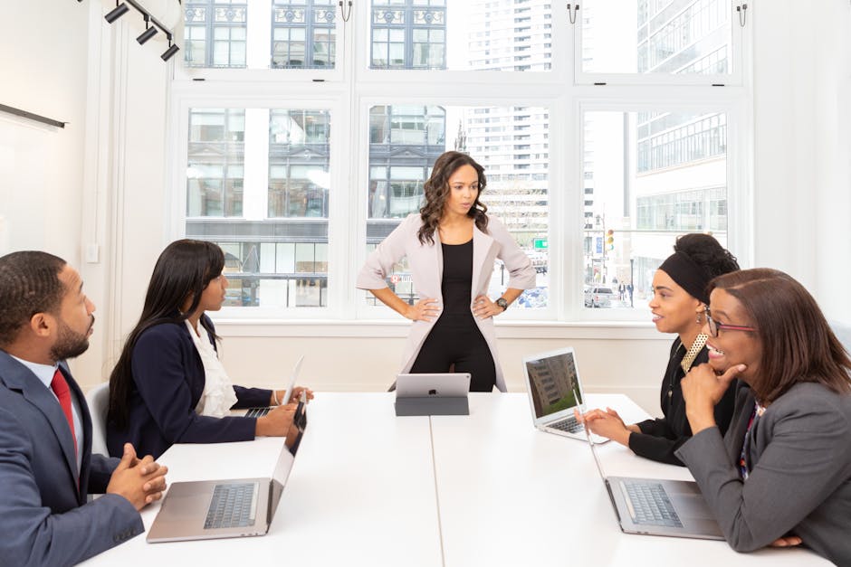 A diverse group of professionals engaged in a meeting at a modern office with laptops and city view
